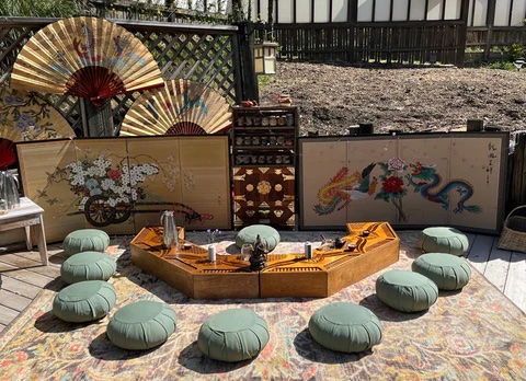 A serene tea lounge with a wooden tea table, sage cushions, and ornate fans