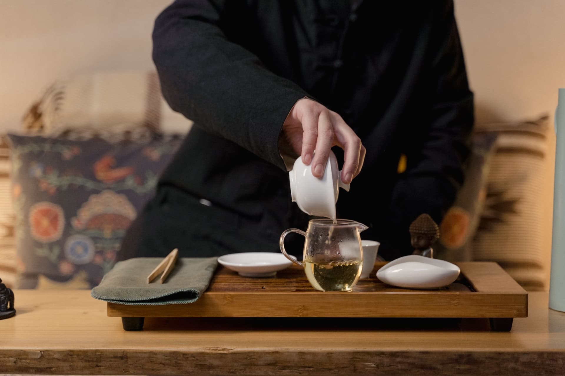 Pouring tea from a gaiwan into a glass pitcher on a bamboo tea tray